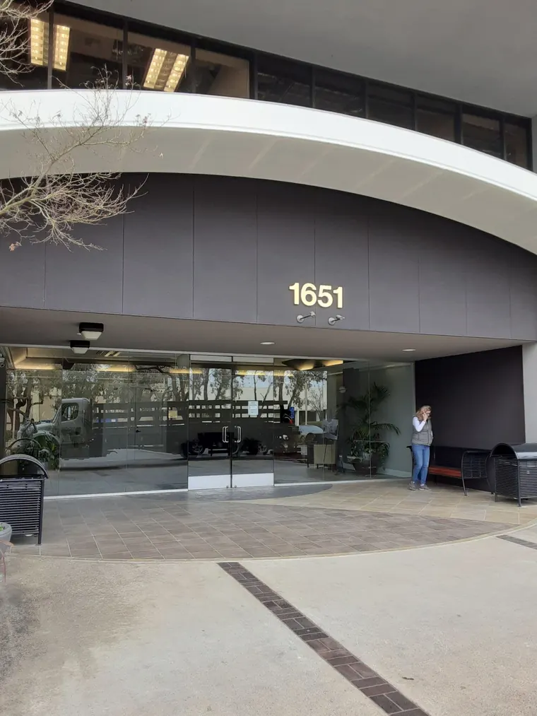 Flat cut-out 1651 address numbers mounted on the dark fascia above the glass entrance of the office building