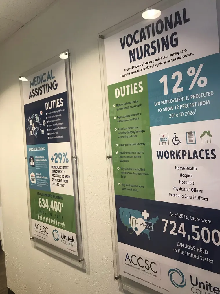 Medical Assisting and Vocational Nursing information prints behind clear acrylic on standoffs in a hallway